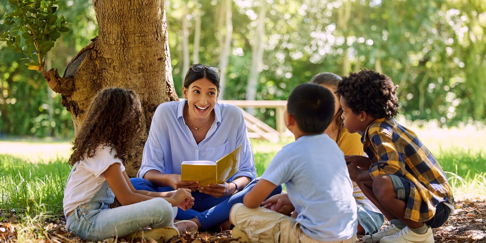 teacher reading with students outdoors beside tree