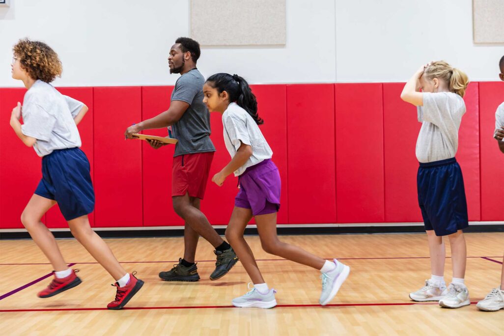 smsu_ms-physical-edu-coaching-sport_image-1 Physical Education teacher helping young kids get active in the gym